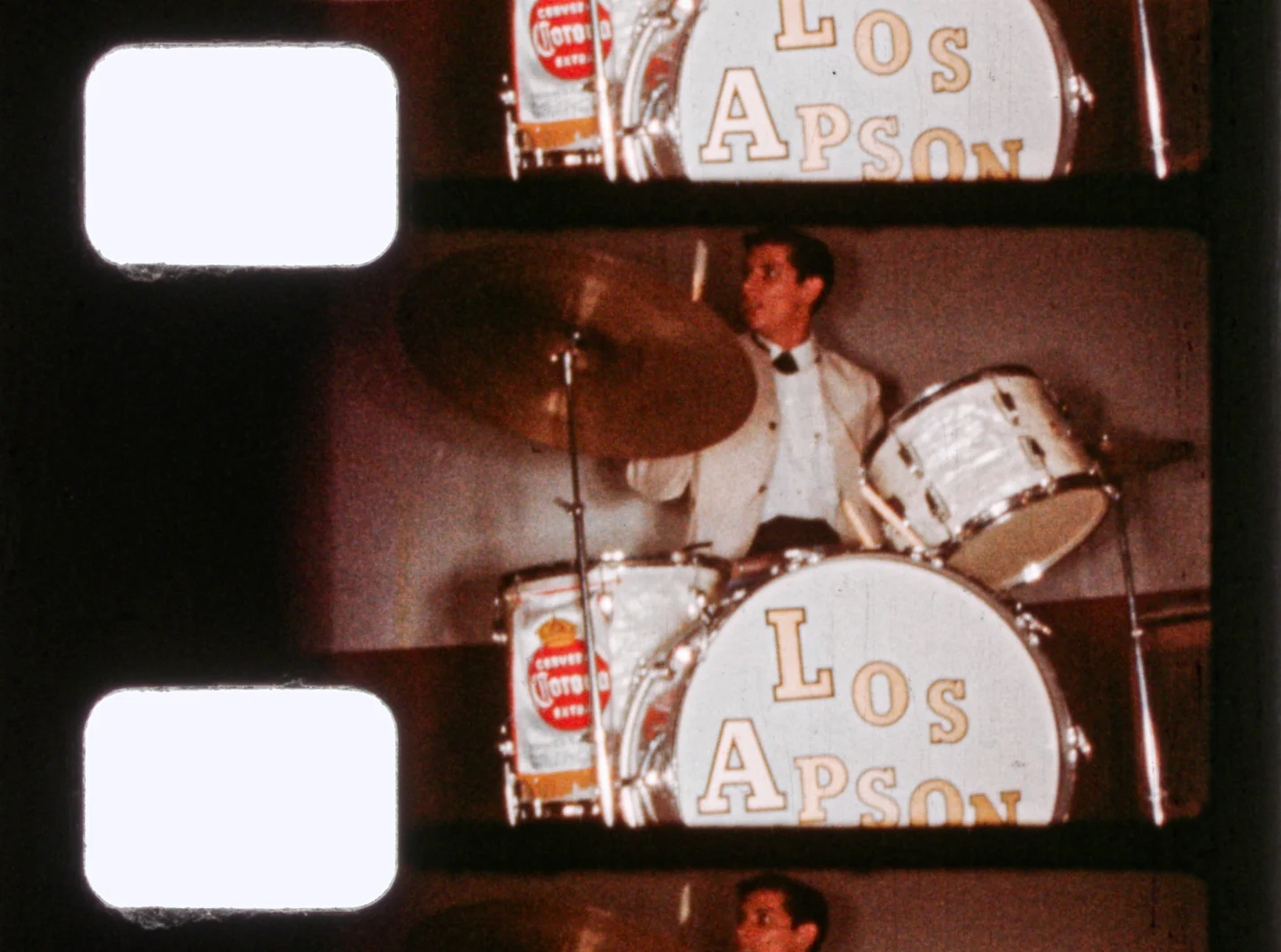 Fotograma de 8mm con perforaciones: el baterista de Los Apson detrás de un bombo con el logo de Cerveza Corona.